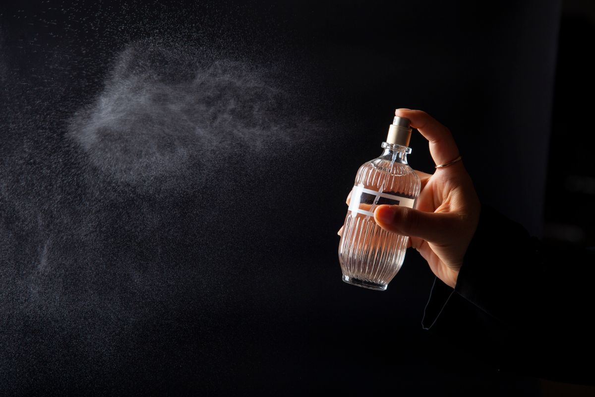 A hand elegantly spritzing perfume from a decorative bottle against a dark background.