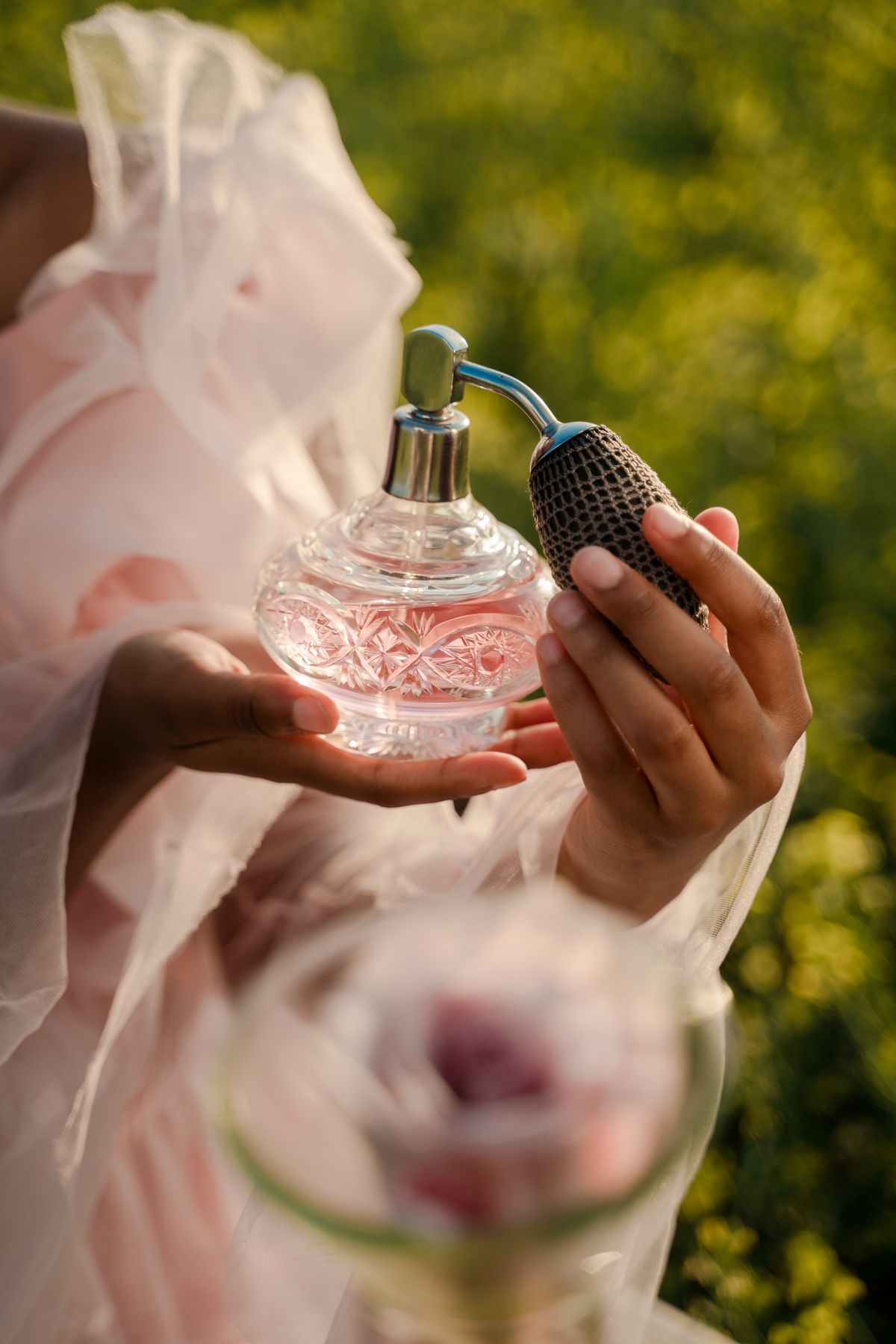 Woman holding a vintage perfume bottle in a field with floral background.