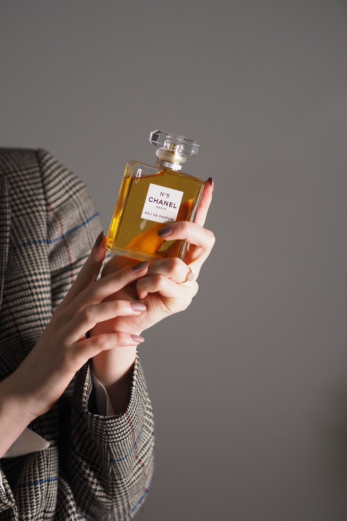 Close-up of hands holding Chanel No. 5 perfume bottle against a soft gray background.