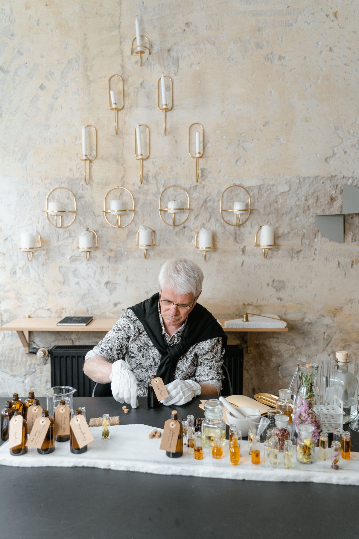 Elderly man creating perfumes in a serene indoor setting with various glass bottles.