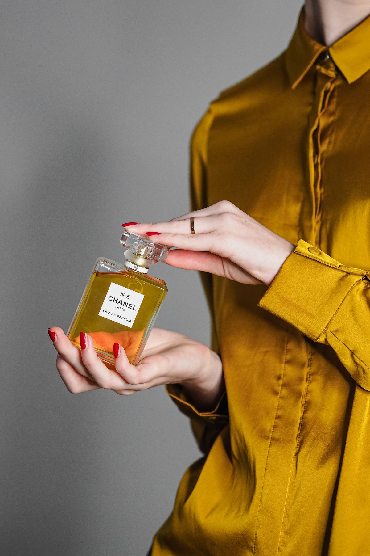 Chic image of a woman holding a Chanel perfume bottle against a gray background.